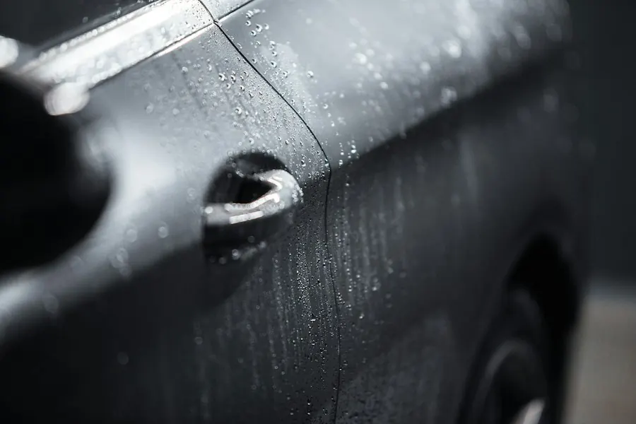 Glossy black car door panel with water droplets
